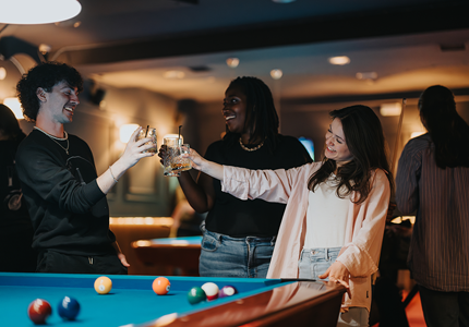 three people having drinks around a pool table